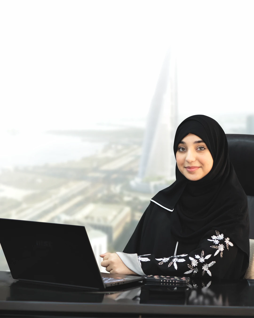 a woman in a black head scarf sitting in a chair with a laptop